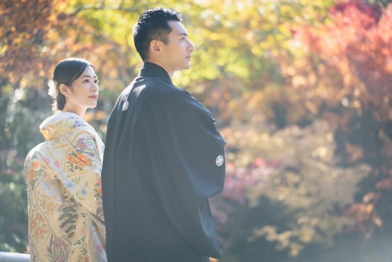 目白庭園の色づいた紅葉を背に、遠くを見つめて並ぶ紋付袴の新郎と色打掛の花嫁。秋の和装前撮り