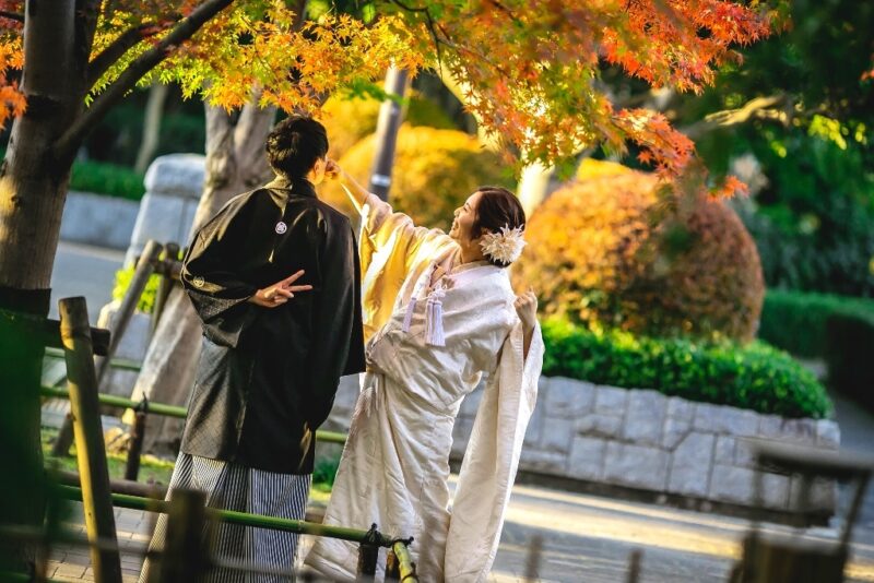 色鮮やかな紅葉の木の下で、楽しげにおどける紋付袴の新郎と白無垢の花嫁。秋の和装前撮り