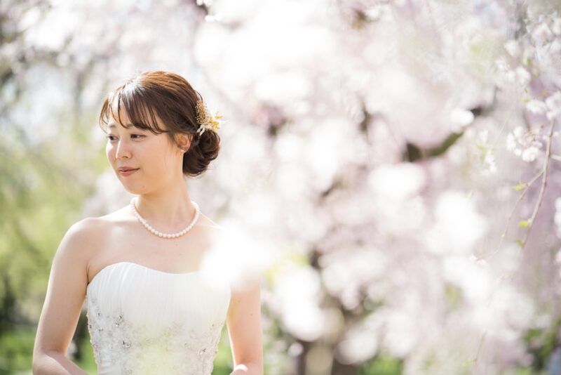 満開の桜を背景にしたウェディングドレス姿の新婦 パールネックレスが上品な一枚