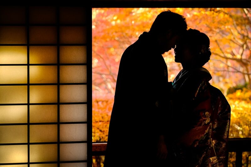 障子の窓辺で紅葉を背に、おでこを寄せ合う新郎と色打掛の花嫁のシルエット。秋の和装前撮り