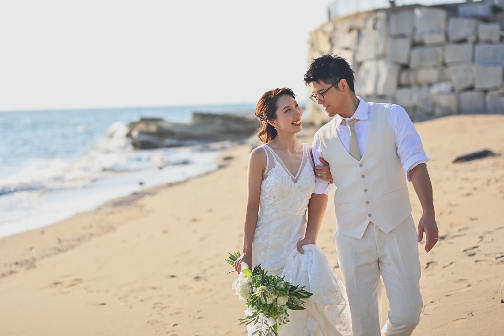 新郎に寄り添い浜辺を歩く夫婦