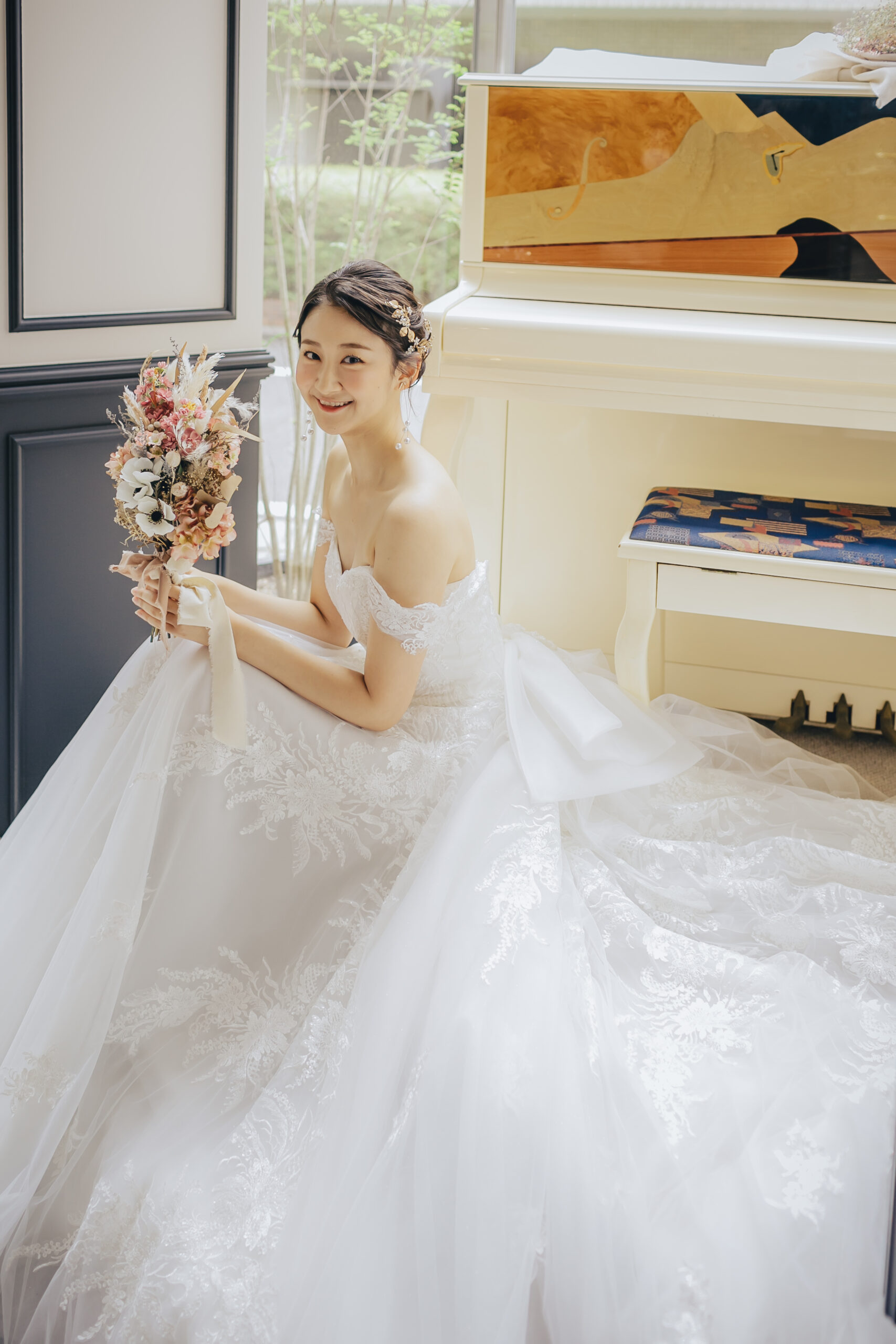 白いアップライトピアノの前でドライフラワーブーケを持つ新婦 オフショルダーレースドレス