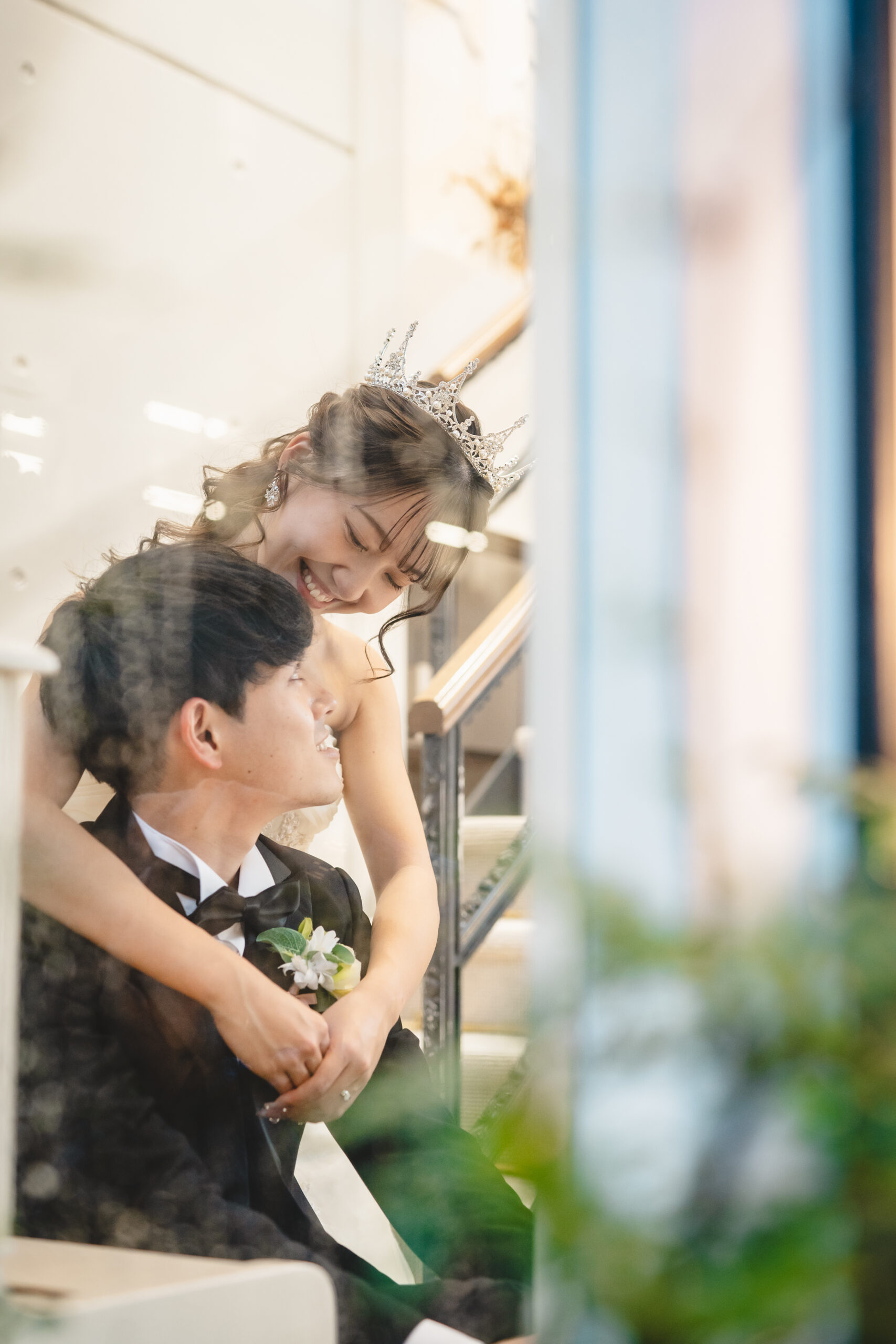 ガラス越しに写る、ティアラを着けた新婦が新郎を優しく抱きしめるロマンチックな一枚