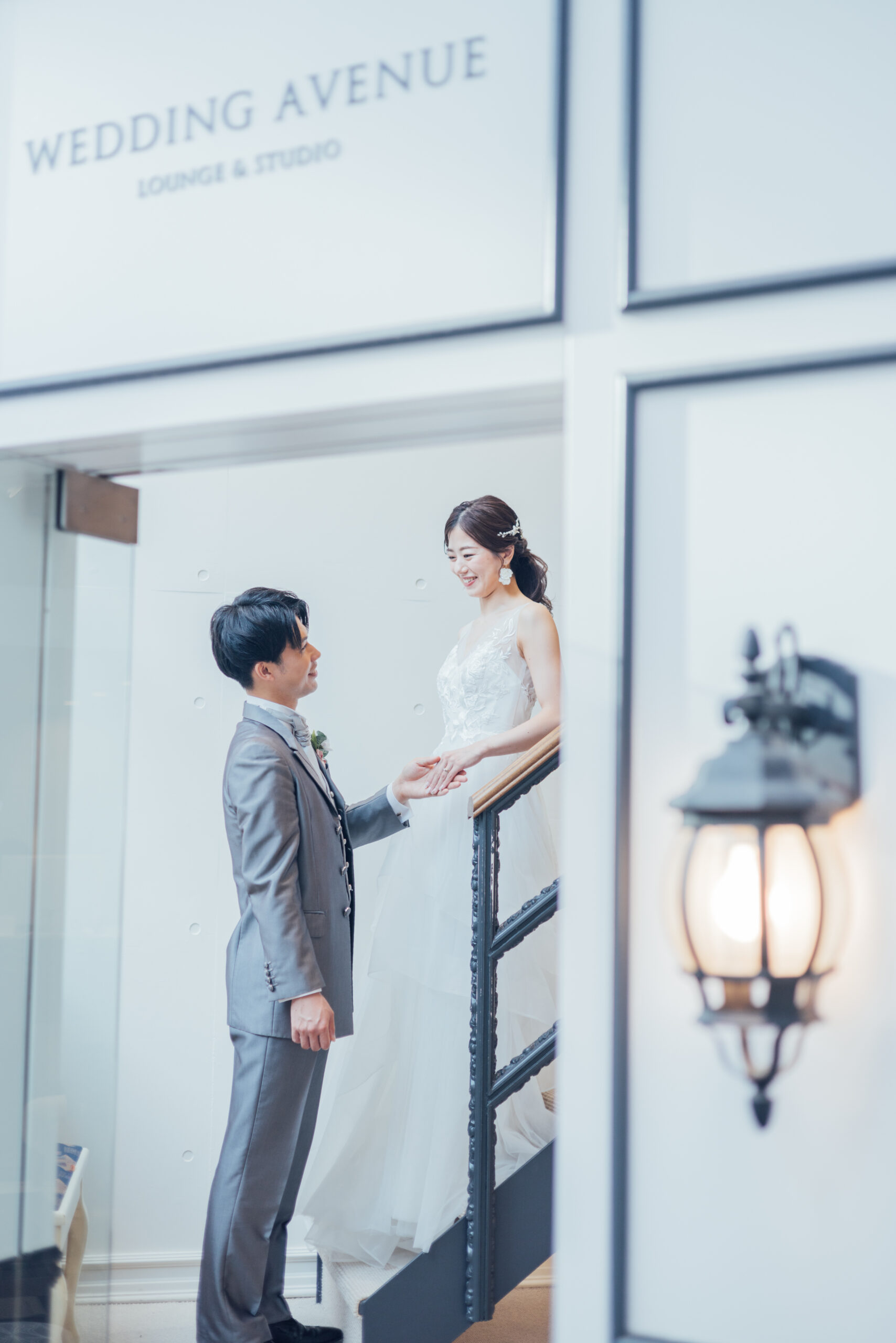 「WEDDING AVENUE」の看板が見える階段で手を取り合う新郎新婦 Vネックレースドレス