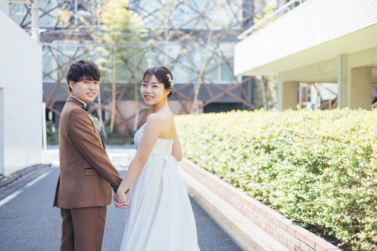 振り返って微笑む新郎新婦 ブラウンスーツとストラップレスドレスの街並みスナップ