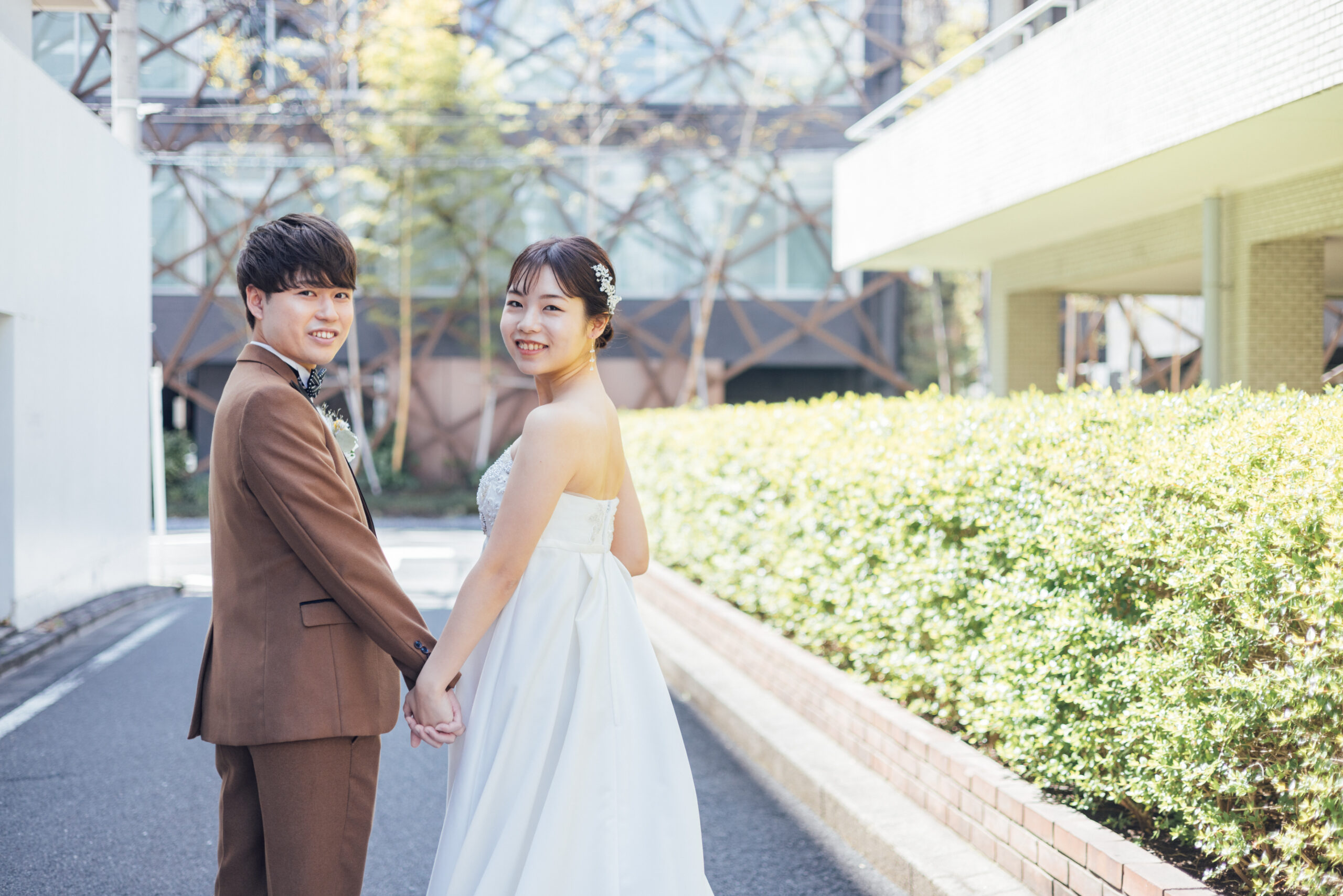 振り返って微笑む新郎新婦 ブラウンスーツとストラップレスドレスの街並みスナップ