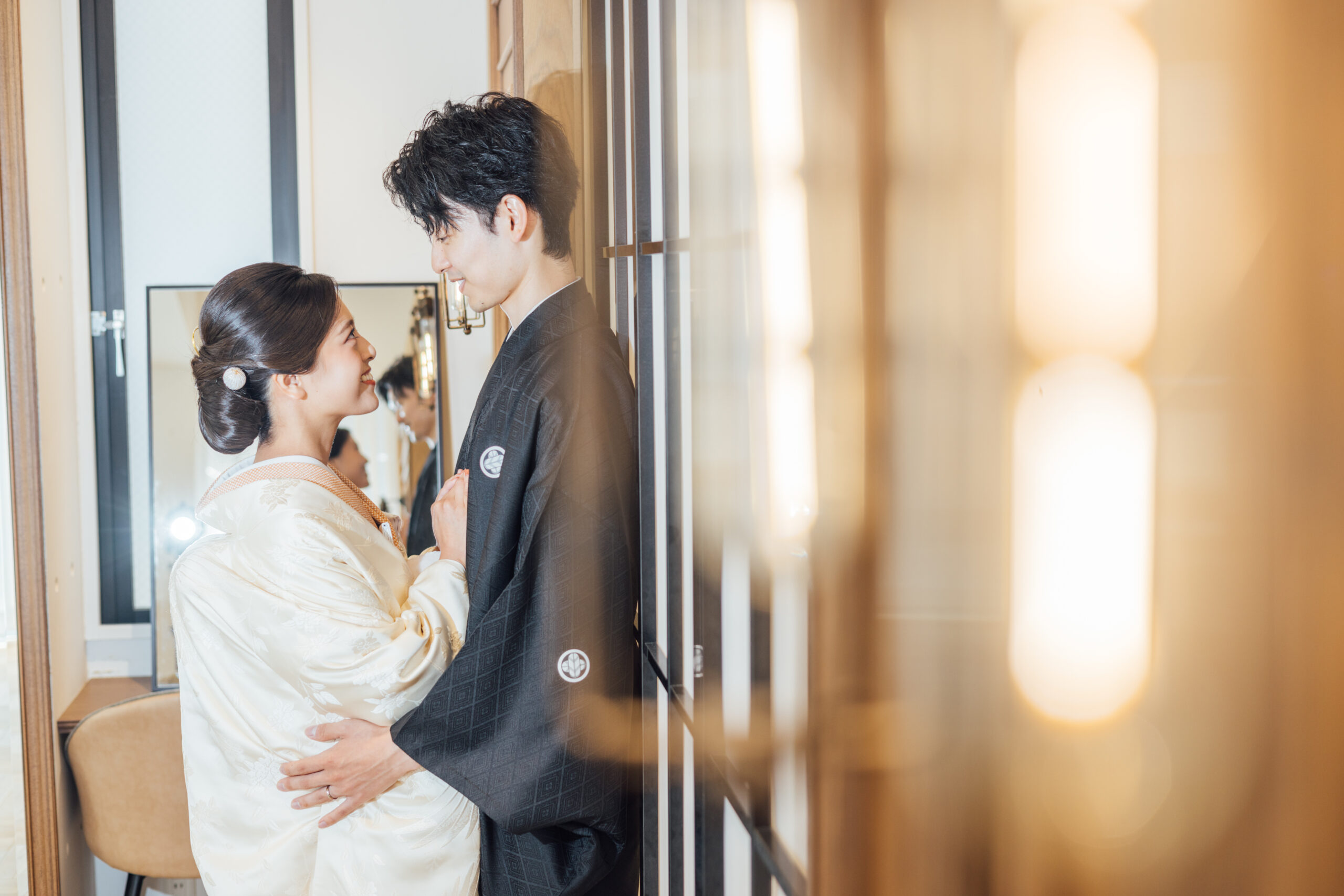 黒紋付袴の新郎と見つめ合う新婦 生成り色の色打掛をまとった鏡前でのひととき