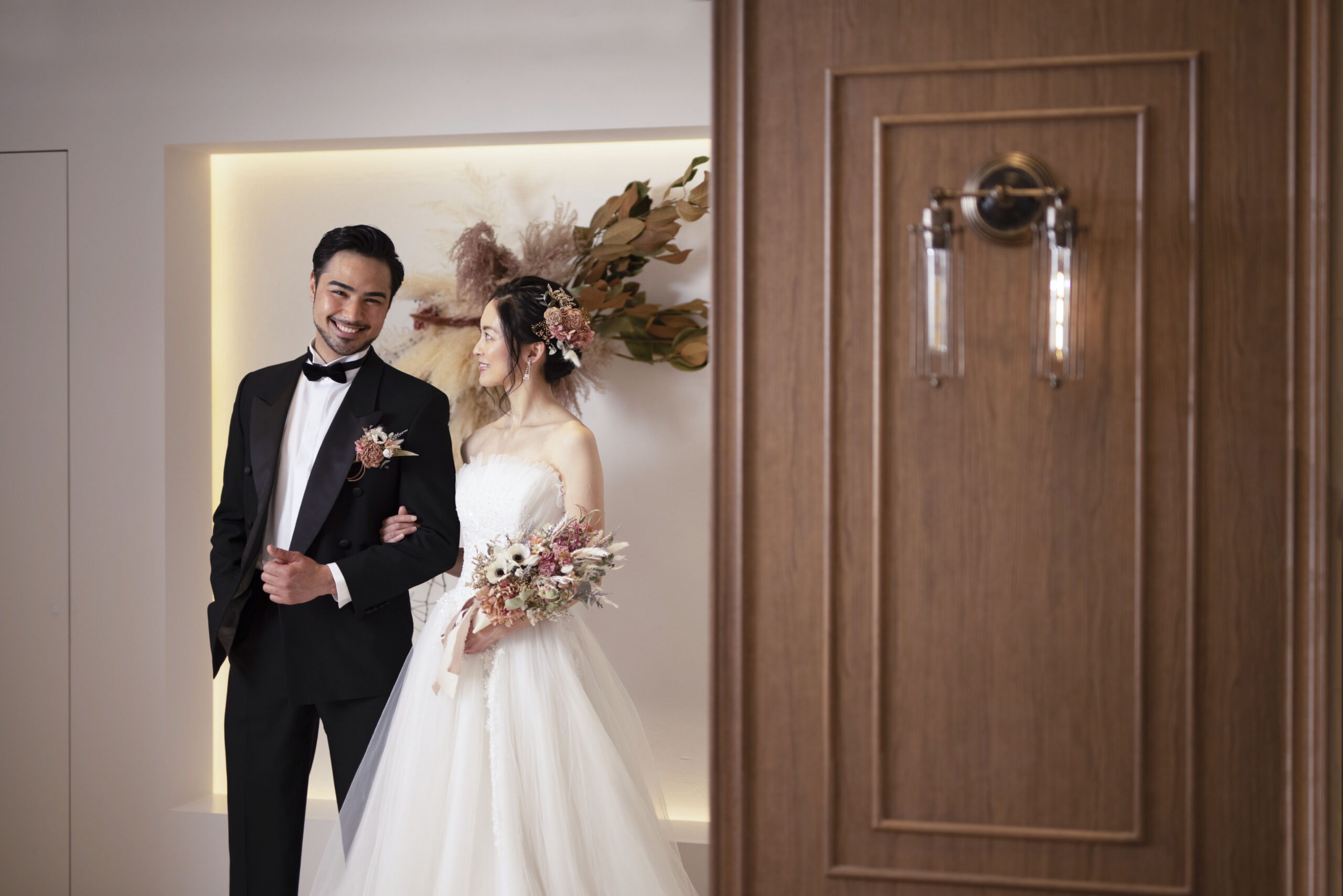 黒タキシードの新郎と寄り添う新婦 パステルカラーのブーケを持つストラップレスドレス姿