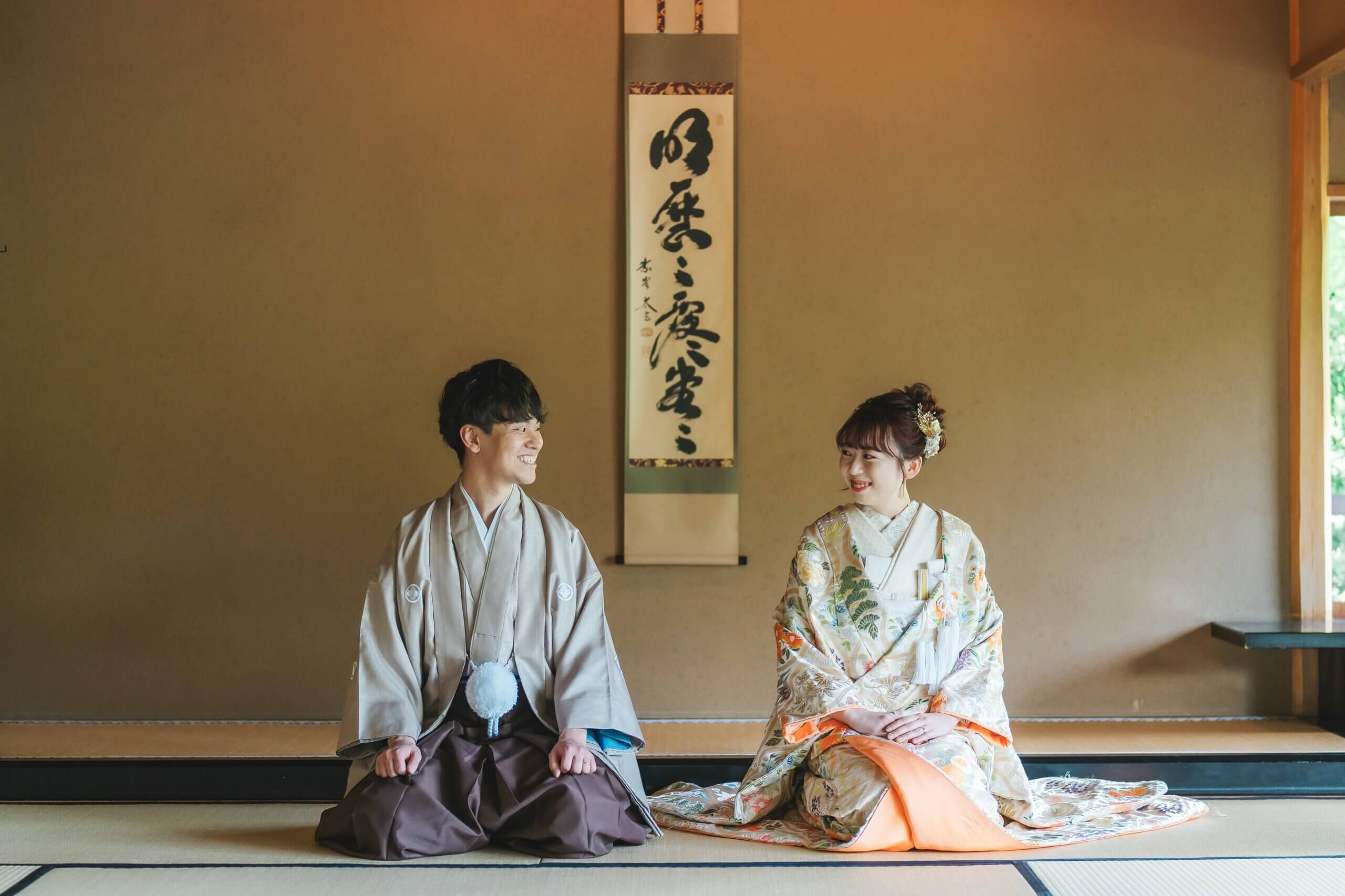掛け軸のある和室で正座して笑い合う目白庭園の和装新郎新婦