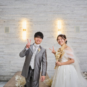 白い石壁の前でそろってピースサインをする新郎新婦。チャペルで撮るポップで楽しいフォトウェディングのポーズ