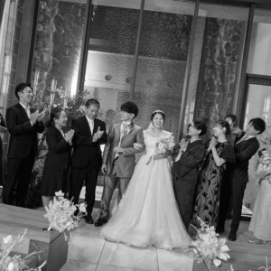 モノクロで撮った、拍手で迎える家族に囲まれて入場する新郎新婦のチャペルフォト。喜びの瞬間を残す結婚写真