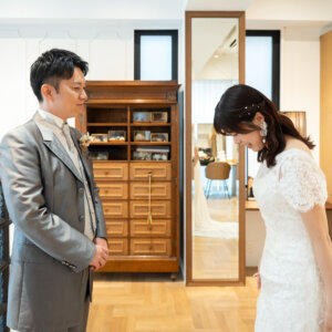 木の扉とアンティークの棚がある部屋で、振り向く前の新郎とうつむく花嫁。ファーストミートの始まりを写した結婚写真