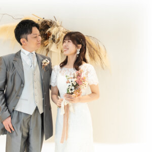 やわらかな光の白い空間で、ブーケを持つ花嫁とグレーのタキシードの新郎が見つめ合うナチュラルなスタジオフォト