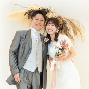 白い壁とドライフラワーのスワッグの下で、頭を寄せ合って笑う新郎新婦。南青山のスタジオで撮る洋装フォトウェディング