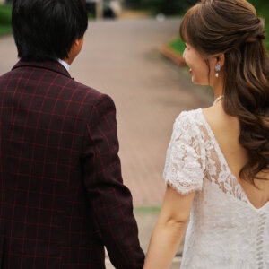 校舎へ続く坂道で手をつなぎ、振り返る花嫁と新郎の後ろ姿。レースのウェディングドレスで撮る学校の前撮り