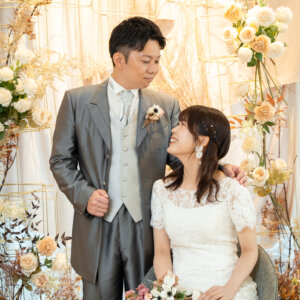 花とドライフラワーで彩られたセットで、座った花嫁と見つめ合うグレーのタキシードの新郎。南青山のスタジオで撮る結婚写真