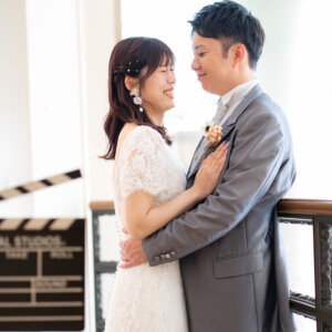 カチンコを置いたアイアンの手すりのそばで、抱き合ってほほえむ新郎と花嫁。映画のワンシーンのような前撮り