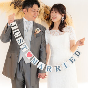 パンパスグラスのスワッグの下で、JUST MARRIEDのガーランドを持って見つめ合う新郎新婦。白い壁の南青山スタジオで撮る洋装前撮り