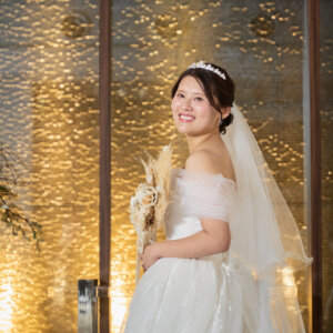ティアラとロングベールを着けたオフショルダードレスの花嫁が振り返って微笑む一枚。金色に輝く壁を背にしたチャペルのウェディングフォト