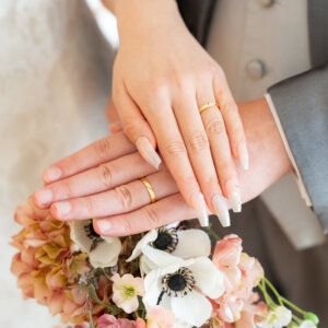 アネモネやくすみピンクの花のブーケに、結婚指輪をはめた手を重ねる新郎新婦の手元。やさしい色合いの結婚写真