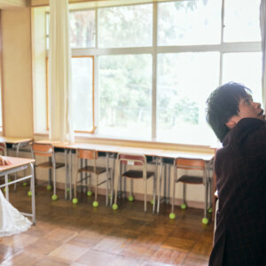 教室の席に座る花嫁と、黒板の上に手を伸ばす新郎。放課後の教室を再現した学校ロケーションフォト