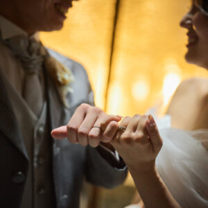 金色の光の中で小指をつなぎ合う新郎新婦の手元。チャペルのあたたかな照明を活かしたウェディングフォト