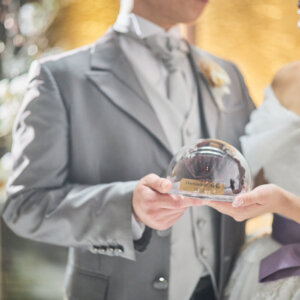 新郎新婦が両手で包み込むガラスのドーム型の記念品を写した手元のカット。チャペルで撮るウェディングフォトの小物ショット