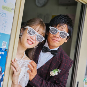 教室の引き戸から顔を出し、おそろいのサングラスで笑う新郎新婦。小物を使ったおちゃめなウェディングフォト