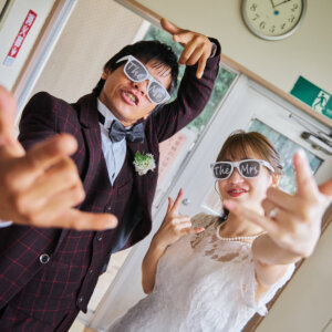 教室の入口で白いサングラスをかけ、カメラに向かってポーズを決める新郎新婦。ノリの良さが伝わる学校ロケーションフォト