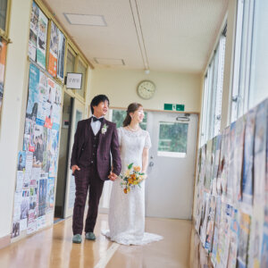 ポスターが並ぶ校舎の廊下を、ブーケを手に並んで歩く新郎新婦。学校の廊下で撮ったナチュラルなウェディングフォト
