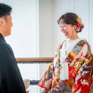 階段の手すりの前で、紋付袴の新郎と向かい合って笑う鶴柄の色打掛の花嫁。南青山のスタジオで撮る和装前撮り