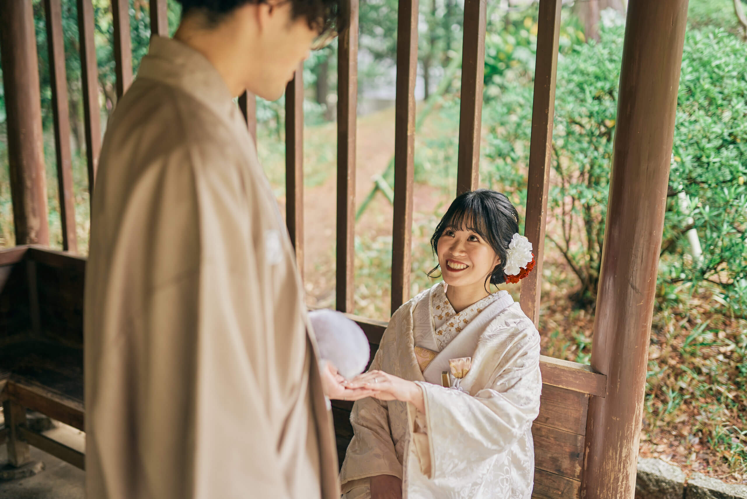 甘泉園公園の木造の東屋に腰かけて肩を寄せ合う白無垢姿の新婦と紋付袴姿の新郎