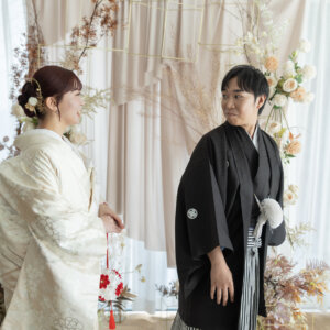 振り返った黒紋付袴の新郎と、毬の小物を手に向き合う白地の色打掛の花嫁。スタジオで撮る和装前撮りのファーストミートの瞬間