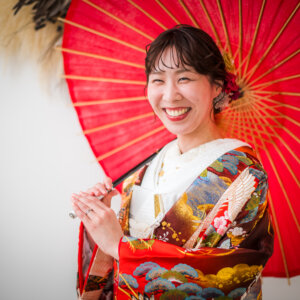 赤い和傘を肩にかけ、笑顔を見せる鶴柄の色打掛の花嫁のアップ。南青山のスタジオで撮る和装前撮り