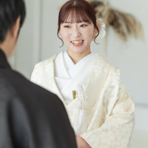 新郎の肩越しに、うれしそうに笑う白地の色打掛の花嫁。スタジオで撮る和装前撮りのファーストミートで生まれた自然な笑顔