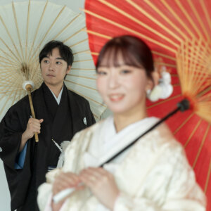 赤い和傘の花嫁と白い和傘の新郎を手前から写した、奥行きのある構図。南青山のスタジオで撮る和傘を使った和装前撮り