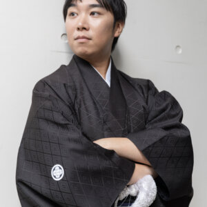 白い壁の前で腕を組み、遠くを見る黒紋付袴の新郎。南青山のスタジオで撮る和装前撮りの、かっこいい新郎ソロのポーズ