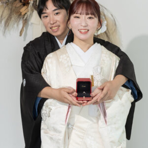 後ろから花嫁を抱きしめ、二人で指輪のケースを手にする紋付袴の新郎と白地の色打掛の花嫁。南青山のスタジオで撮る和装前撮り