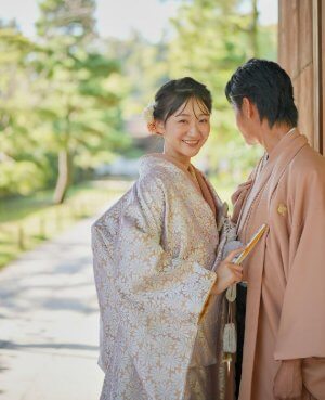AMOS16 花華金白のウェディングドレス。白い花模様を一面に散りばめた可憐な色打掛。細やかな意匠が織りなす優美な世界観に、動くたびきらりと覗くゴールドの裏地が花嫁心をそっとくすぐる。華やかさと上品さを兼ね備え、晴れの日をより格別に彩る特別な一着。