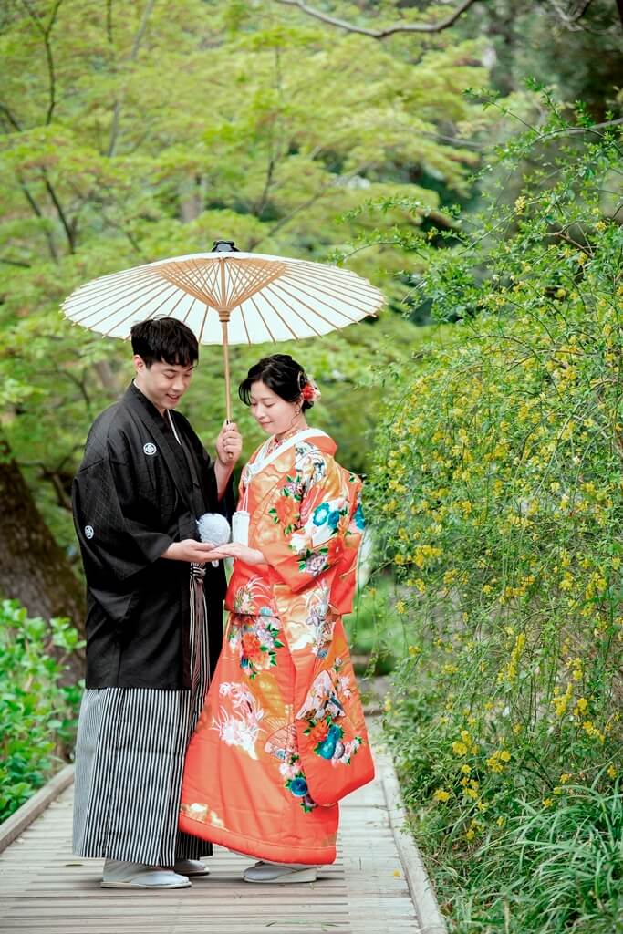 甘泉園公園の庭園で色打掛の袖口を口元に添えて微笑む新婦の写真